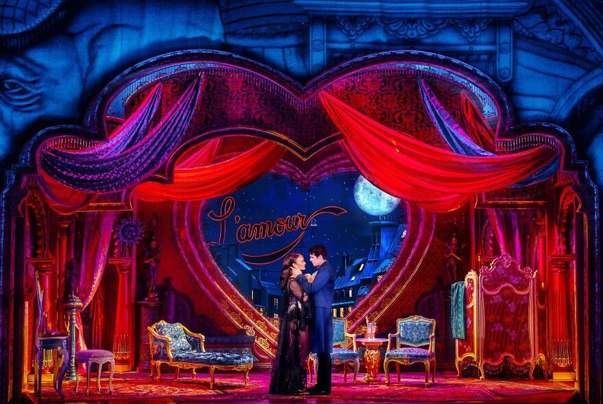 Moulin Rouge stage set with two performers centre stage in an embrace surrounded by theatre props.