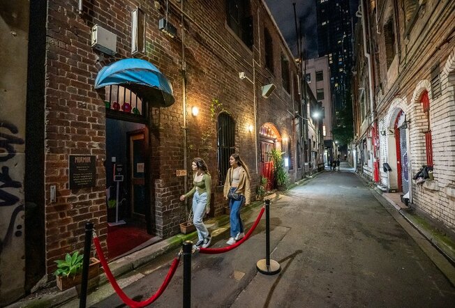 Two women walking into a laneway venue at night,