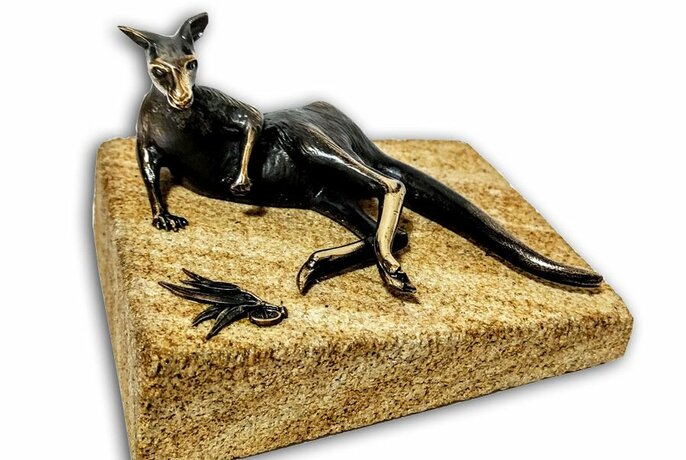 Pewter sculpture of a kangaroo resting on a small stone base.