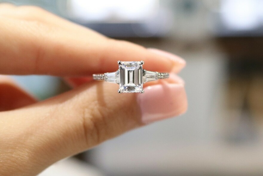 Side view of fingers holding a diamond ring.
