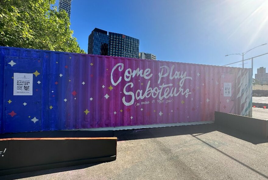 Exterior of converted shipping containers showing a painted sign that reads 'COME PLAY SABOTEURS'.