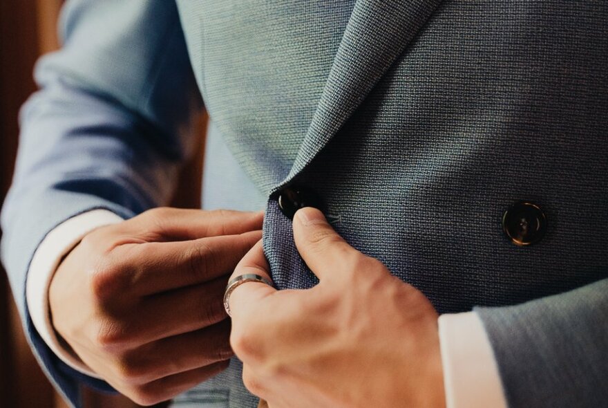 Hands buttoning buttons on a grey suit.