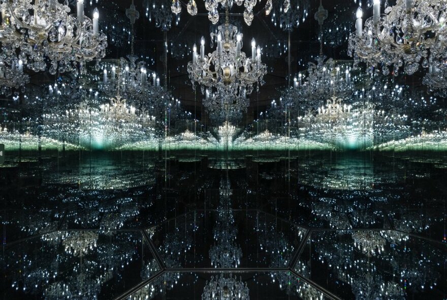 An immersive installation in a large gallery room featuring mirrors and glass chandeliers hanging from the ceiling.