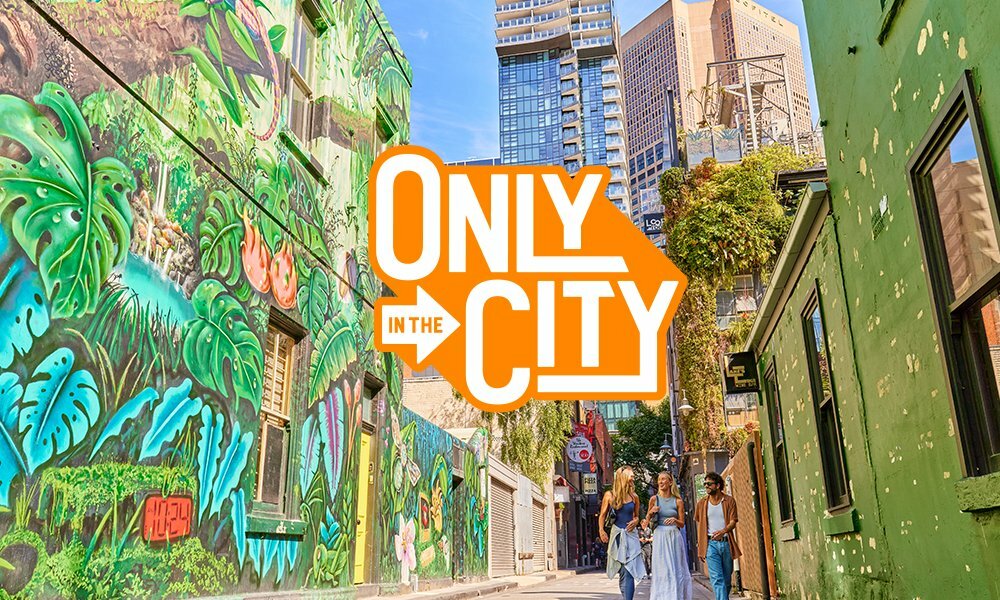 People walking through a laneway with street art. A text overlay reads 'only in the city'.