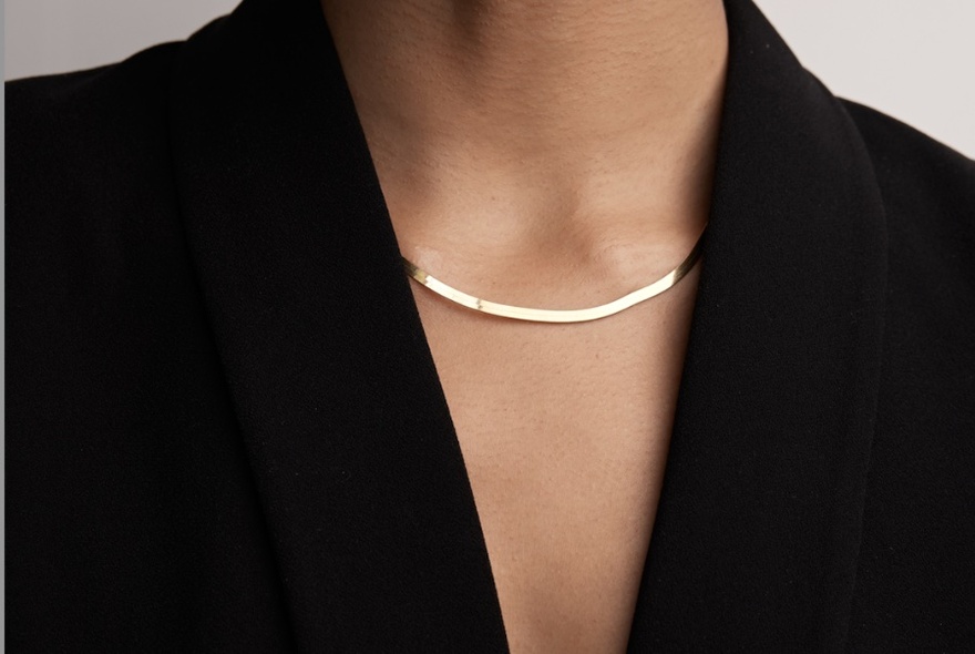Close-up a woman's neck displaying a thick flat gold necklace.