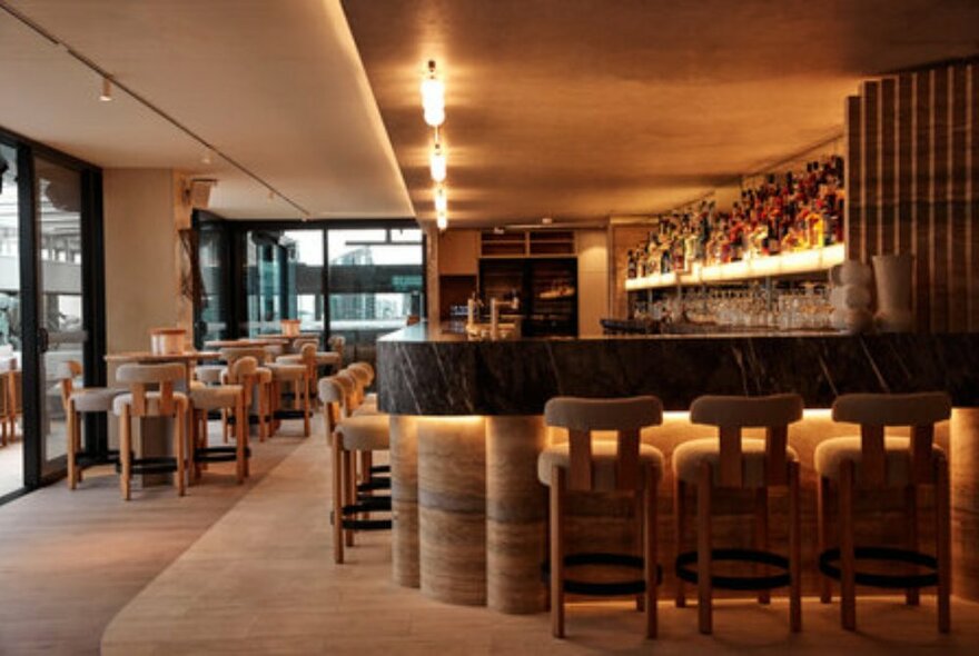 The internal bar of Fleet Rooftop Bar, with muted colours, a curved bar and padded bar stools.