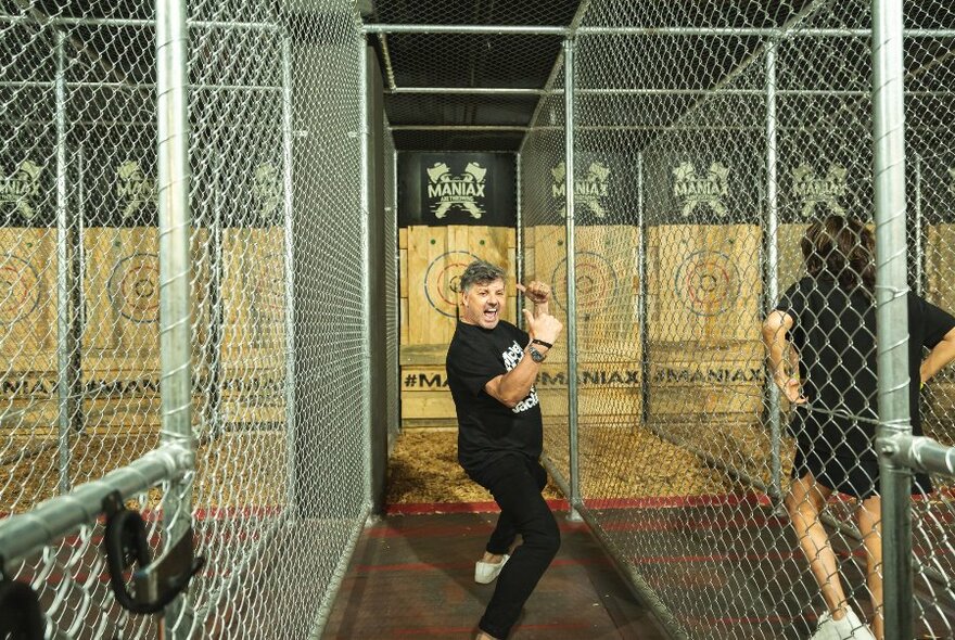 Man standing in a caged and cheering after having just thrown an axe at a wooden wall.