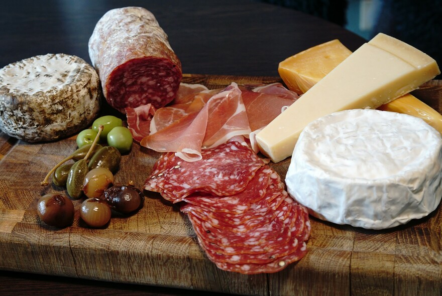 Selection of charcuterie and cheeses, placed on a board.
