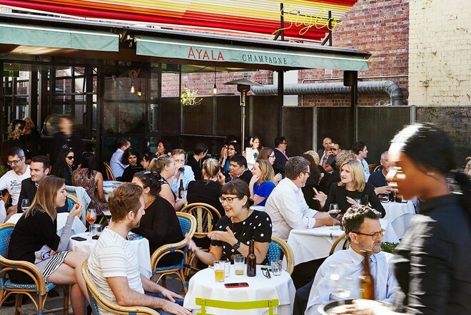 Siglo outdoor area crowded with people eating and talking at tables with wicker chairs.