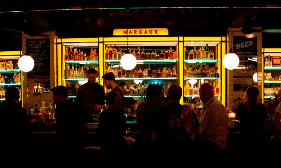 People sitting at a dark bar with neon yellow shelves filled with bottles of alcohol.