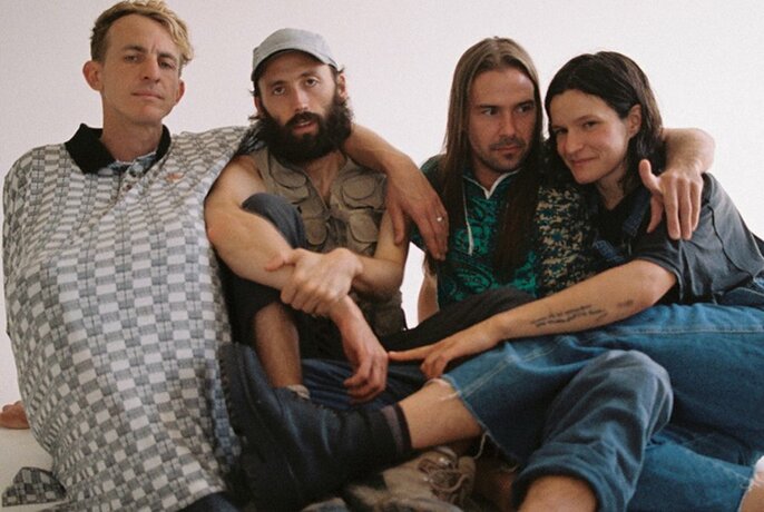 Musical group Big Thief seated on the ground with their arms around each other.