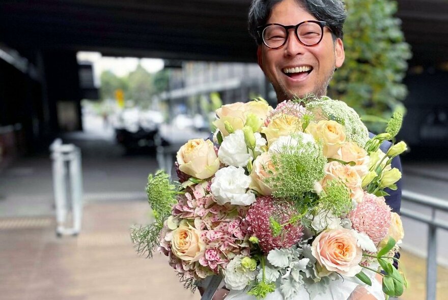 Smiling man wearing glasses holding a big bunch of flowers.