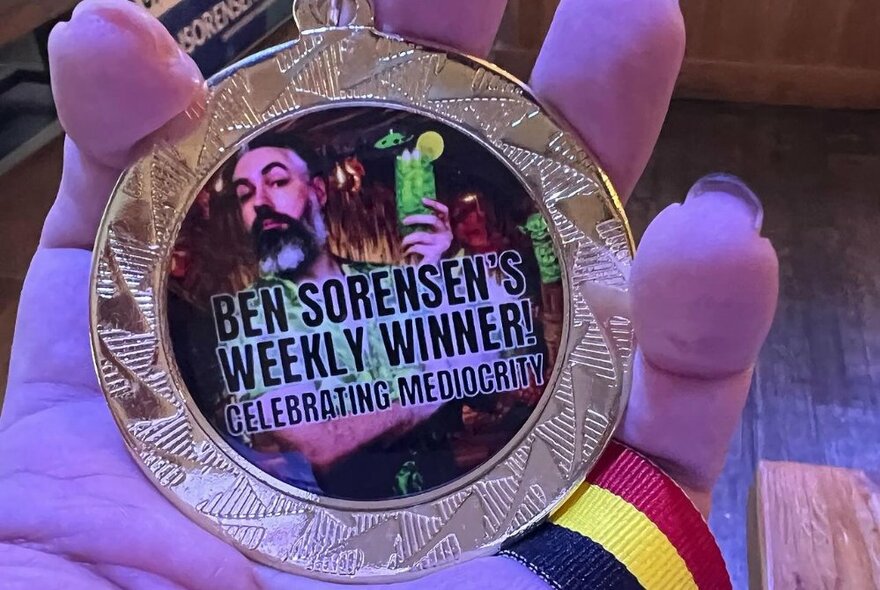 A hand holding a weekly winner medal.
