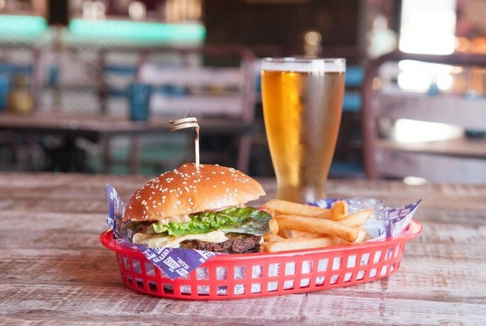 A burger with chips in a basket and a glass of beer. 