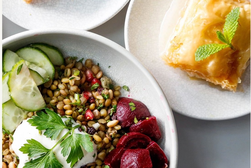 Looking at a bowl of grain salad with yoghurt and a plate bearing a pastry item with a mint garnish. 