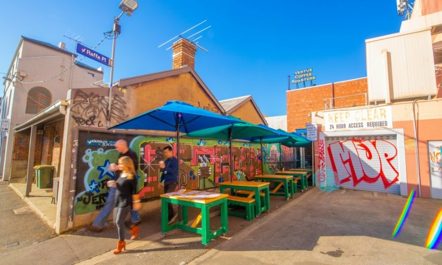 People leaving a hidden cafe with colourful tables, umbrellas and street art.