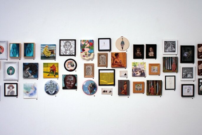 Small framed artworks lining a white wall, arranged in three tiers.