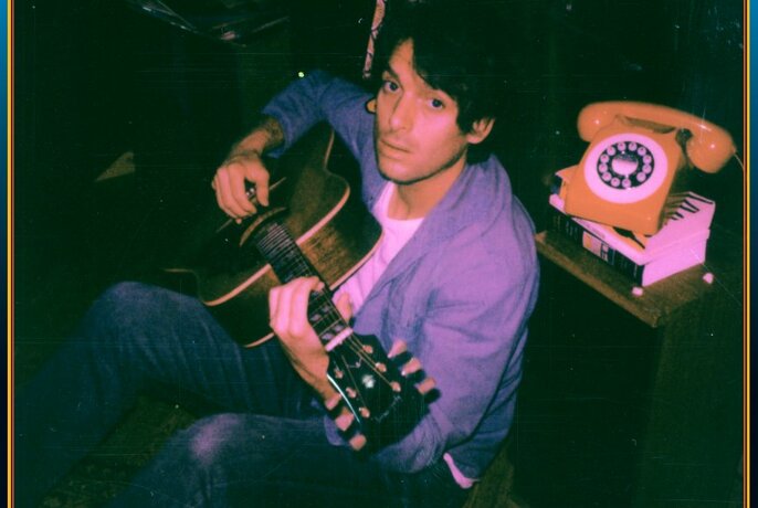Singer and musician Paolo Nutini, playing a guitar next to an old-fashioned yellow telephone.