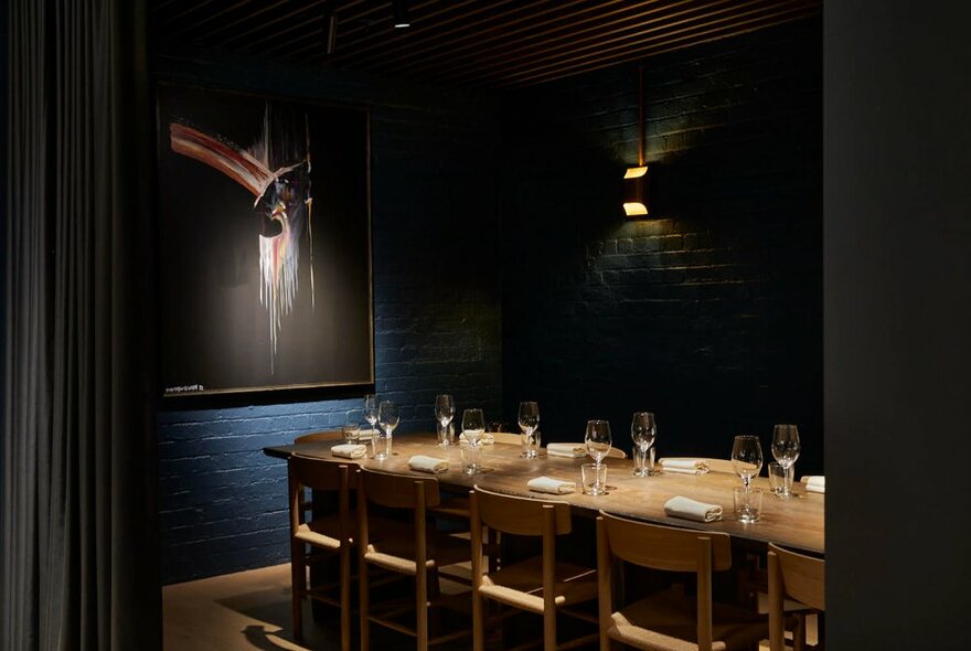 A dark dining room with modern art and a long table.