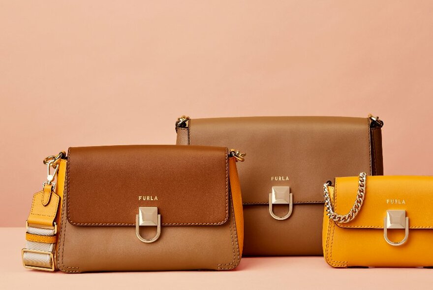 Three handbags in the same style, but differing sizes, two brown and one yellow. 
