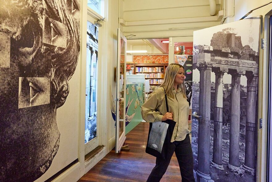 A woman walking out of a bookstore past black and white murals of ancient Greece.