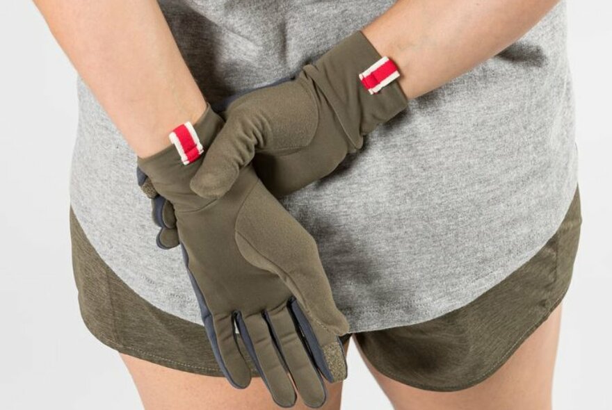 A model dressed in shorts wearing a pair of sporty khaki and red gloves.