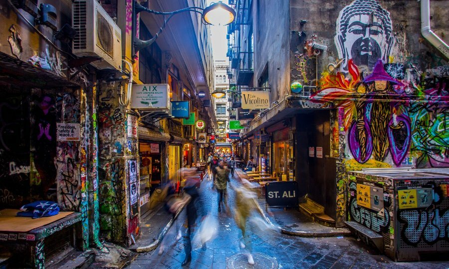 A busy laneway with cafes covered in graffiti. 