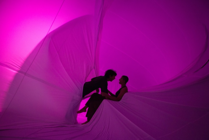 Two dancers facing each other, inside a giant pink inflatable.