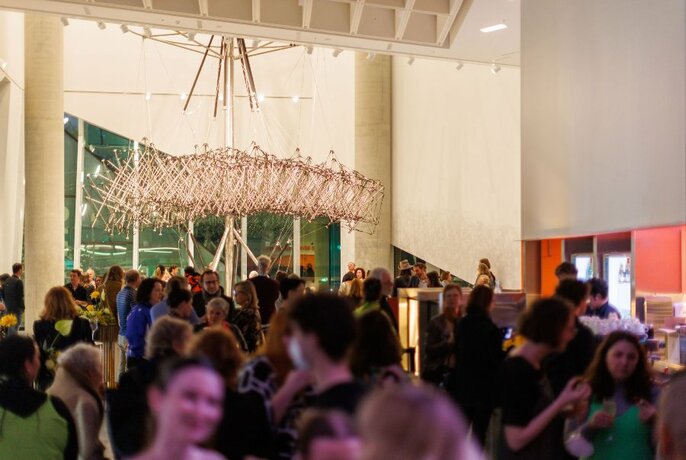 Crowd of people milling about and talking in the foyer area of the Science Gallery, a large hanging sculpture visible in the background.