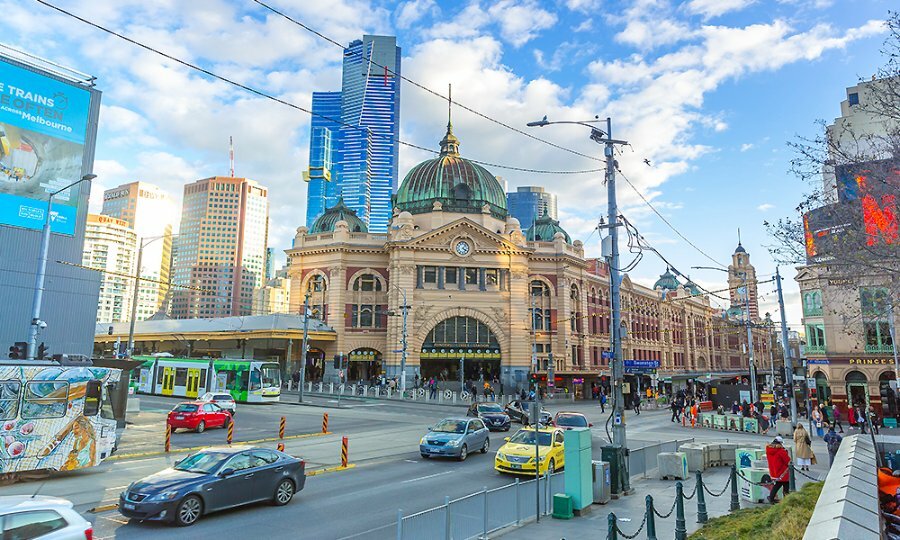 Cars and trams passing in front of Flinders Street Station.