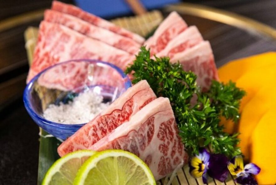 Slices of raw wagyu beef and lemon slices.