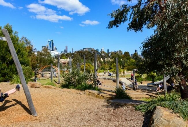 A playground with trees and natural surroundings and children playing. 