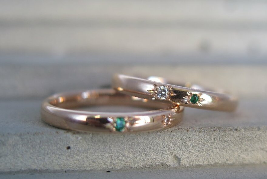 Two rings of rose gold with small inset stones on stone surface.