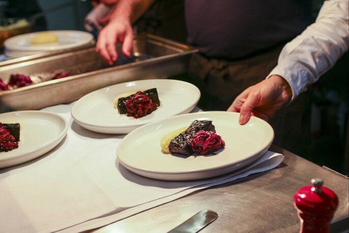 Waiter taking a plate of steak from a food serving area.