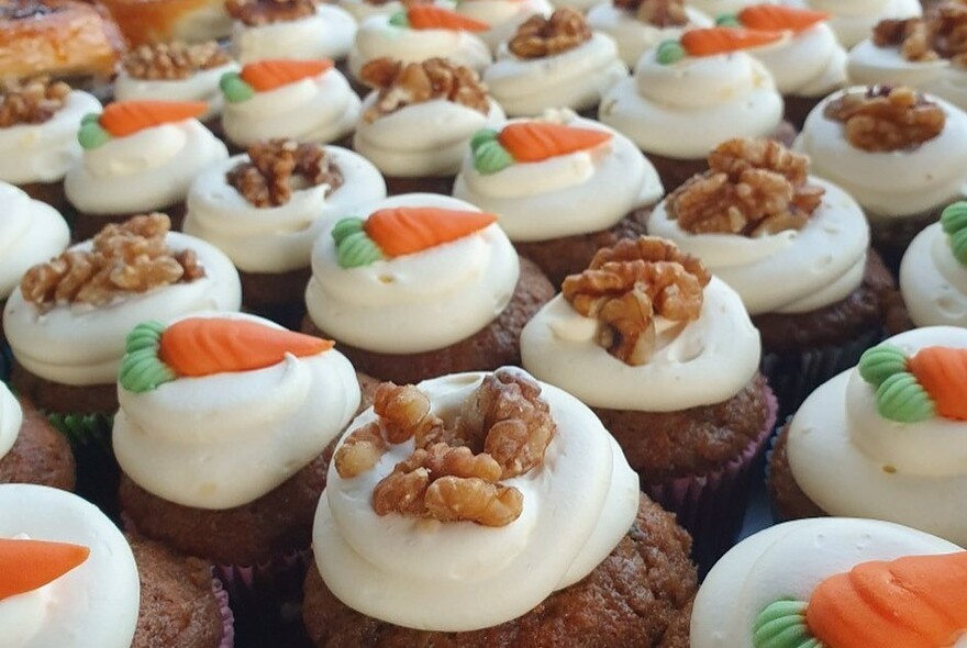 Rows of muffins topped with white icing and marzipan carrots or walnuts.