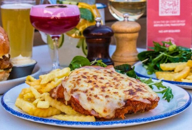 A chicken parma on a plate in front of a cocktail