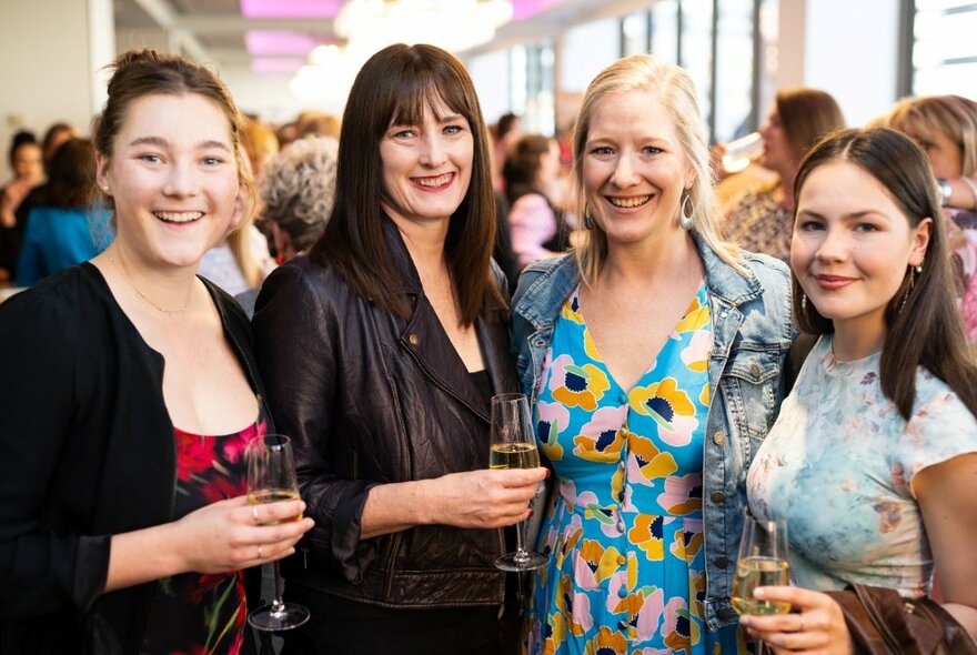 Four women holding glasses of wine at a crowded event.