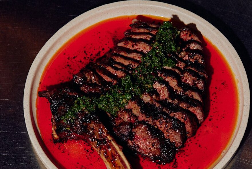 A dinner plate of slices of rare beef with a salsa verde garnish on top, and a red sauce around the sides.