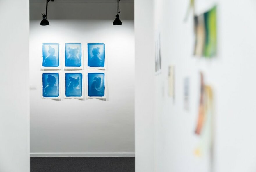 Blue photographic artworks displayed on a white wall.