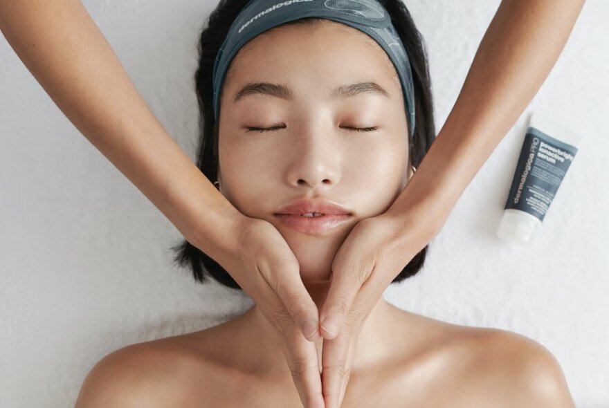 Hands massaging a customer's face with treatment cream.