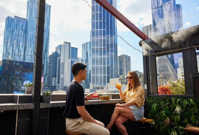 A couple sitting at a rooftop bar drinking colourful cocktails
