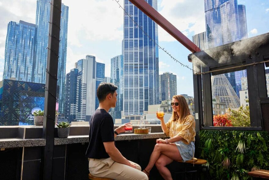 A couple sitting at a rooftop bar drinking colourful cocktails