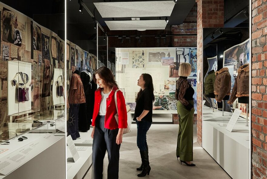 Three women walking through an exhibition showcasing military clothing.