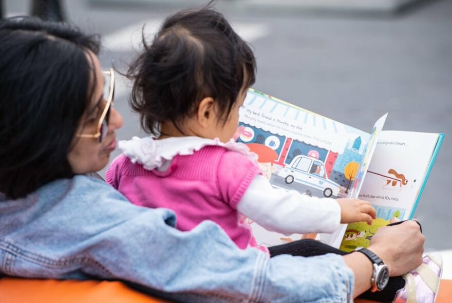 Young toddler sitting on the lap of their parent or carer and turning the pages of a picture book.