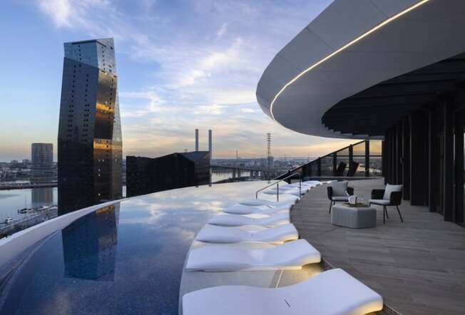 A rooftop infinity pool with day beds overlooking the city.