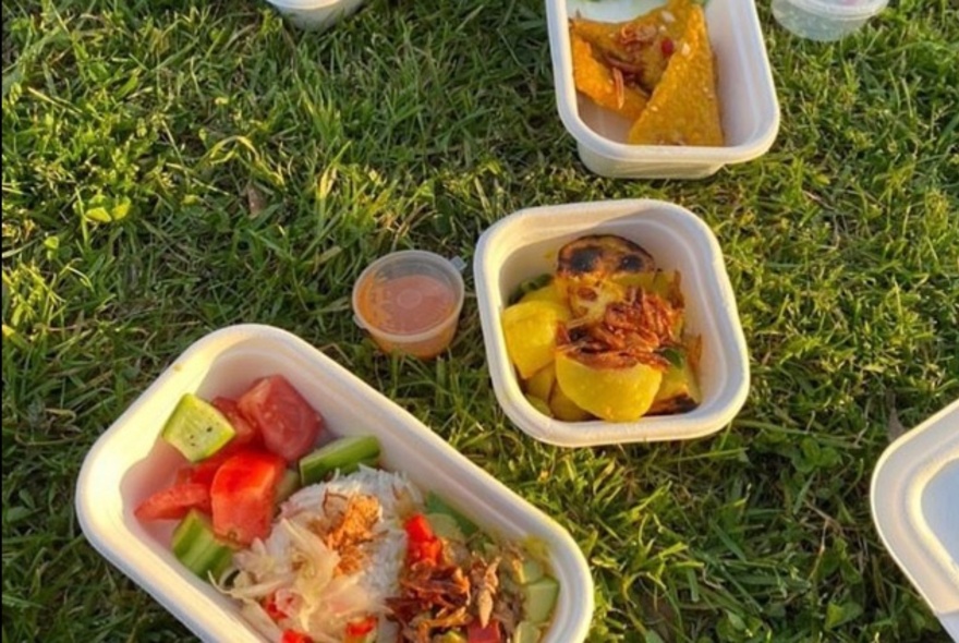 Takeaway containers of Balinese food enjoyed  picnic-style on a lawn.