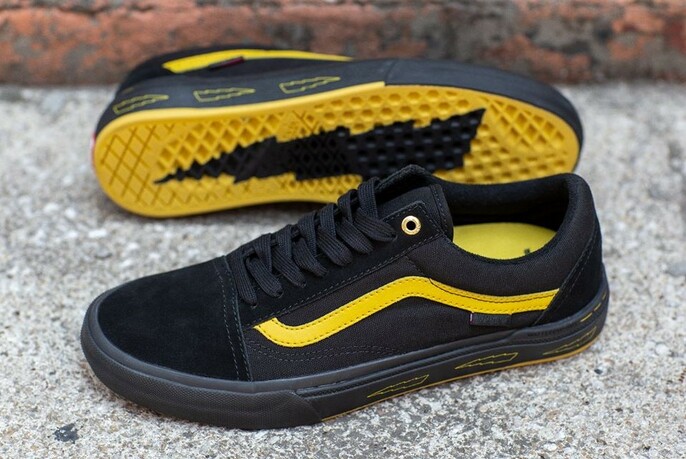 Pair of black sneakers with yellow, curved stripe; sole of one visible - yellow with black lightening strike.