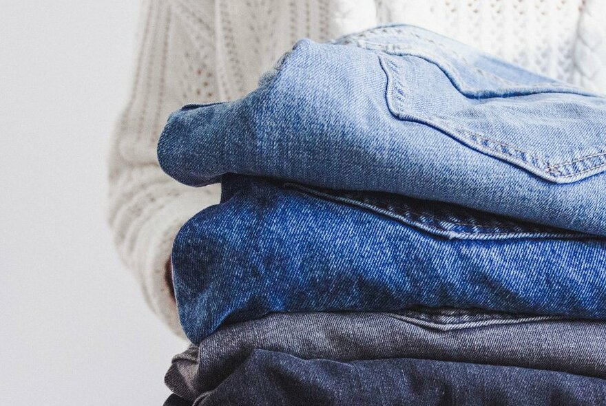 A person holding a stack of denim jeans in various shades of blue.