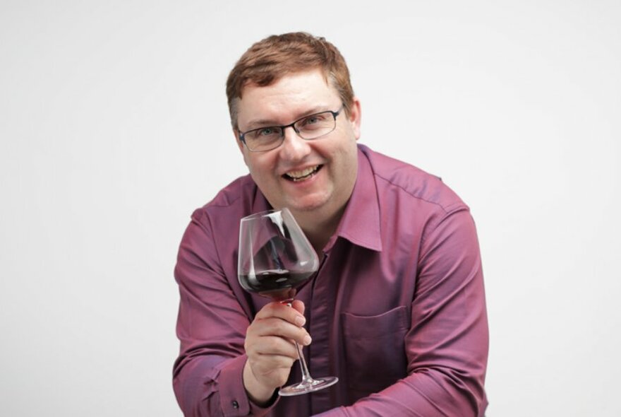 Man wearing a maroon long sleeve shirt and holding a glass of red wine in front of him.