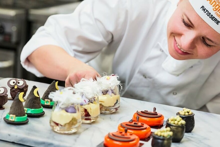 Chef adding details to rows of decorated cakes and desserts.